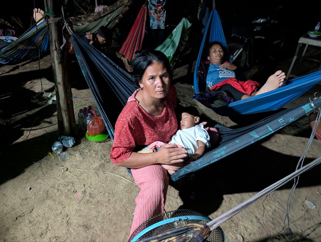 A mother holds her sleeping child as families rest in hammocks at night.